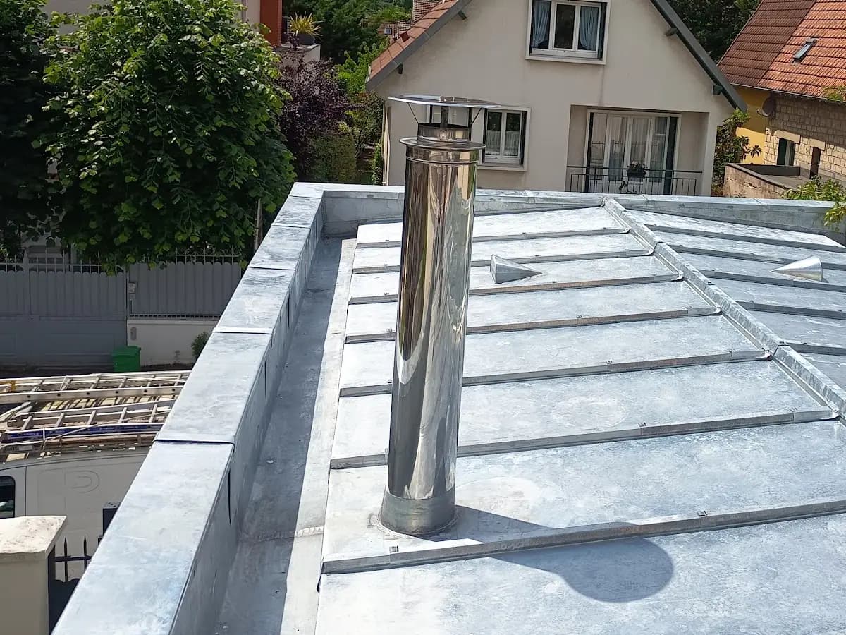 Couverture zinc terminée avec sortie de conduit inox et solin, quartier pavillonnaire en arrière-plan
