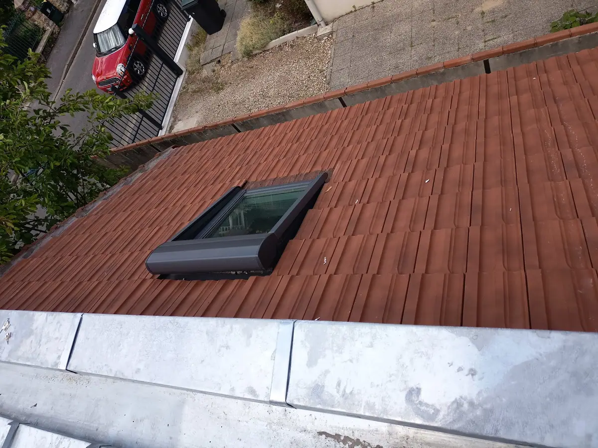 Fenêtre de toit posée sur une couverture en tuiles neuves, vue plongeante depuis le faîtage
