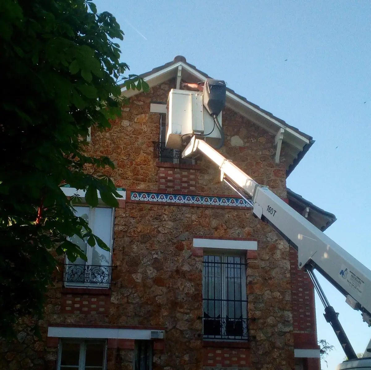 Nacelle élévatrice déployée le long du pignon d’une maison en meulière pour intervenir sur la rive de toit
