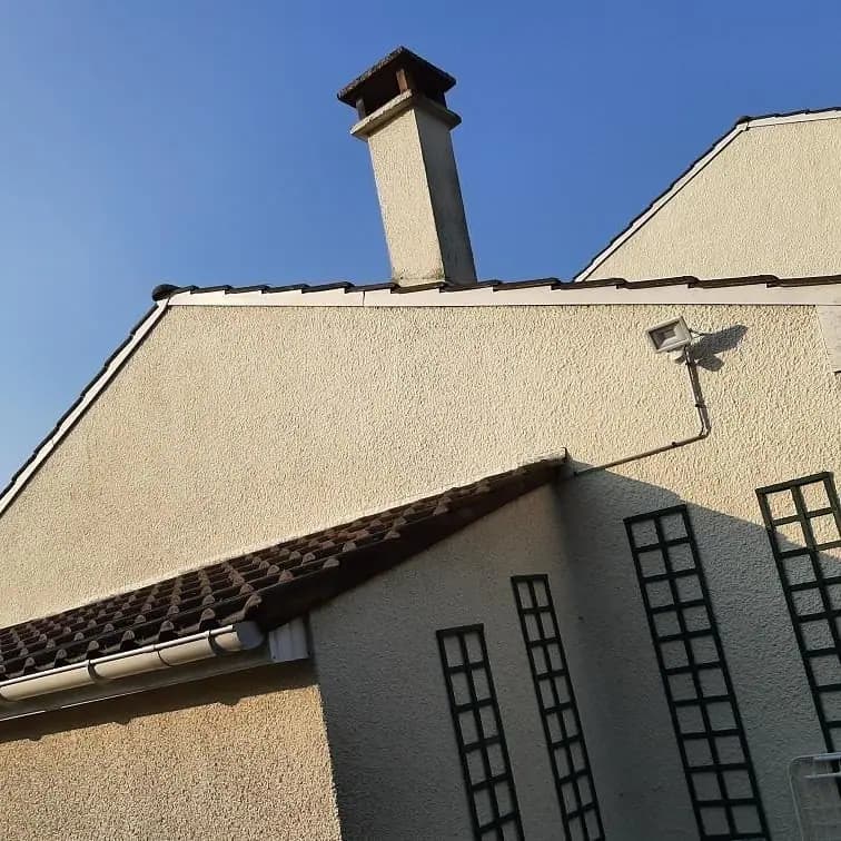 Pignon et rive de toiture en tuiles avec souche de cheminée enduite et gouttière neuve, façade claire