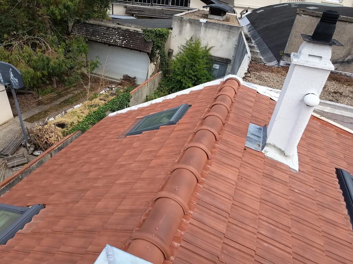 Couverture en tuiles neuves avec faîtage rond scellé, souche enduite et fenêtre de toit